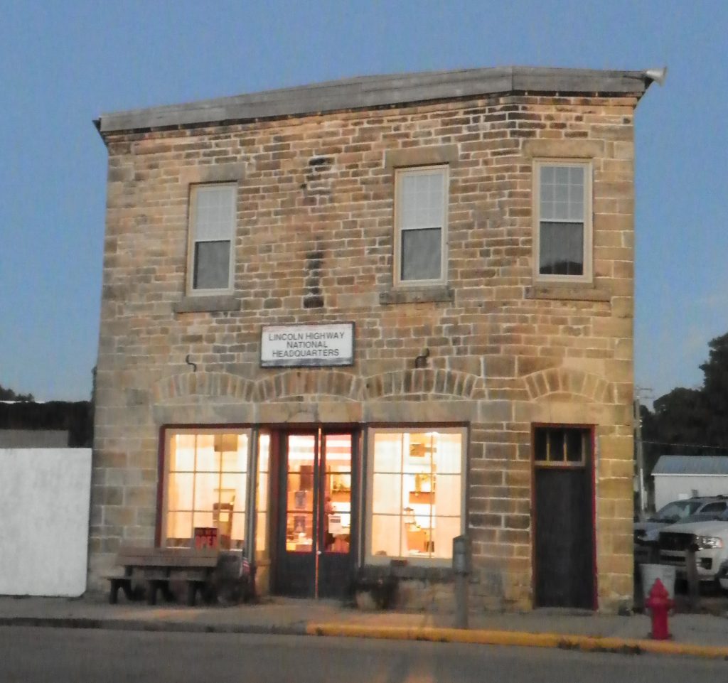 This is an image of the brick H. I. Lincoln Building at dusk, with the lights on inside with some cars parked to the side.